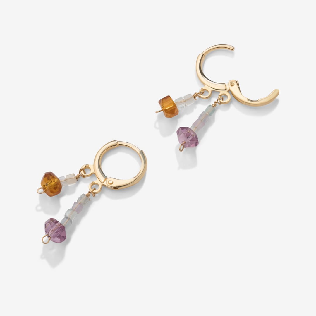 Gold huggie hoop earrings with amber and purple gemstone drops, white background